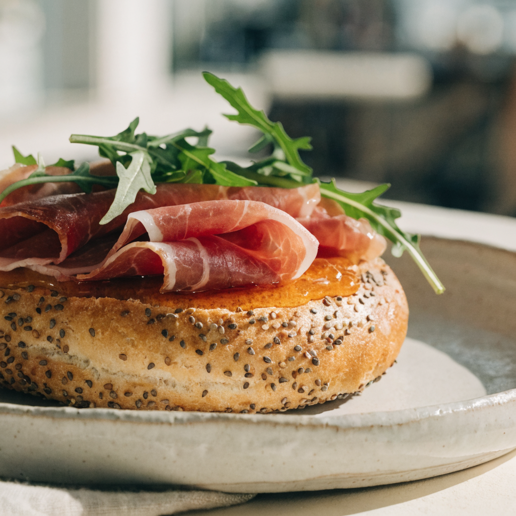 Open-faced bagel layered with prosciutto, arugula, and a drizzle of hot honey