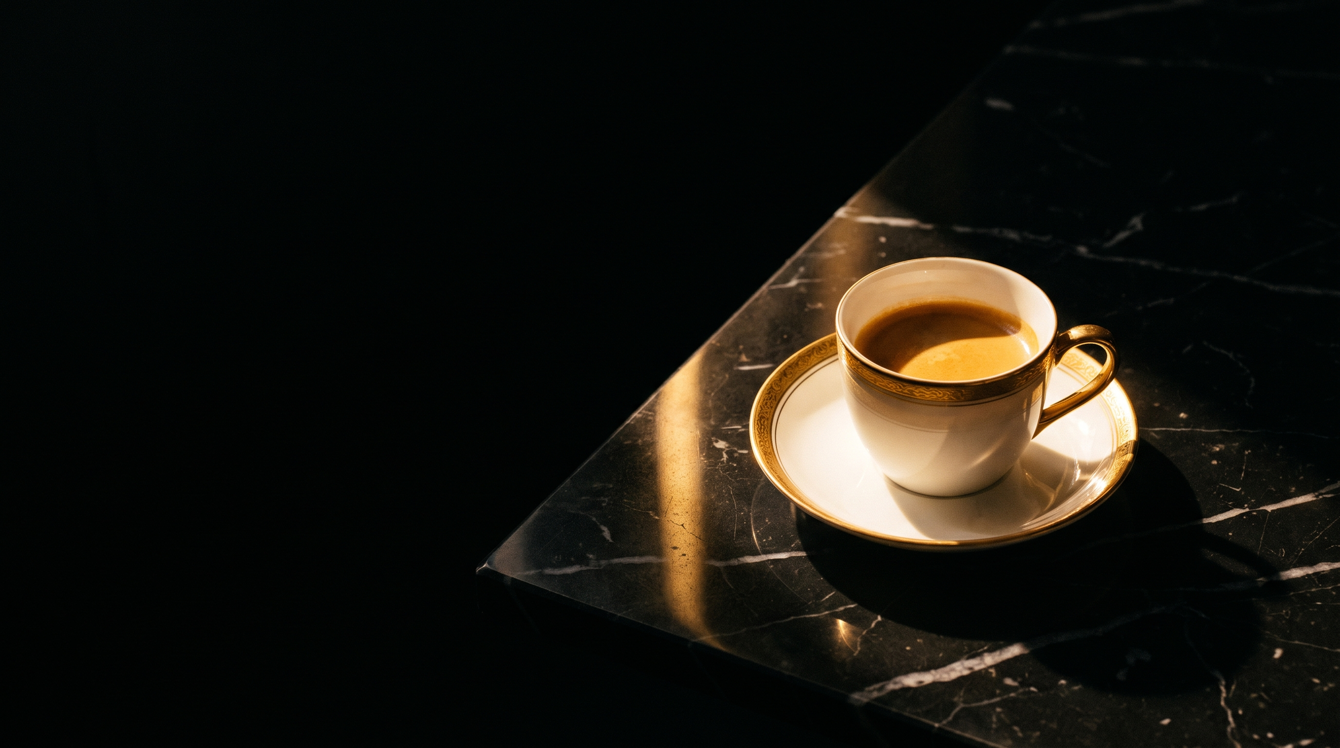 Espresso in a gold rimmed porcelain cup on black marble, struck by a single bar of warm light