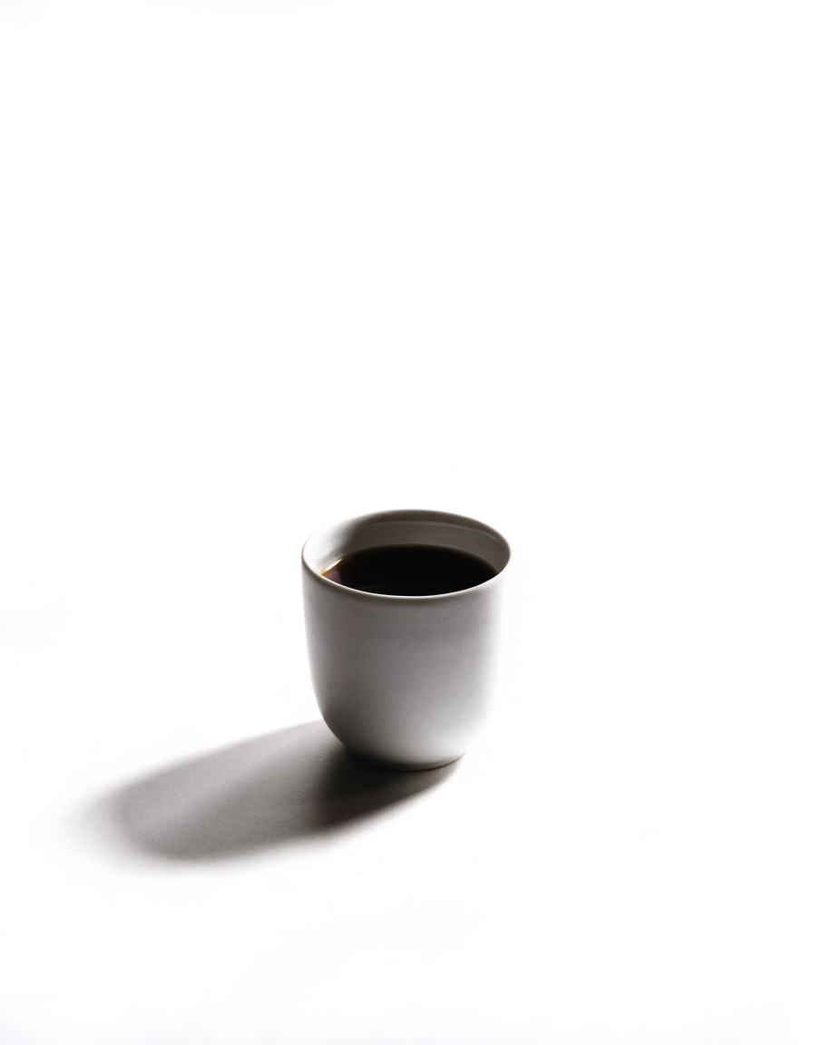 a single white cup of black coffee on a white table